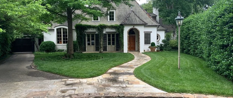 A charming home featuring a stone pathway leading to the entrance, surrounded by lush greenery and well-manicured lawns, set in a tranquil neighborhood with a decorative lamppost.